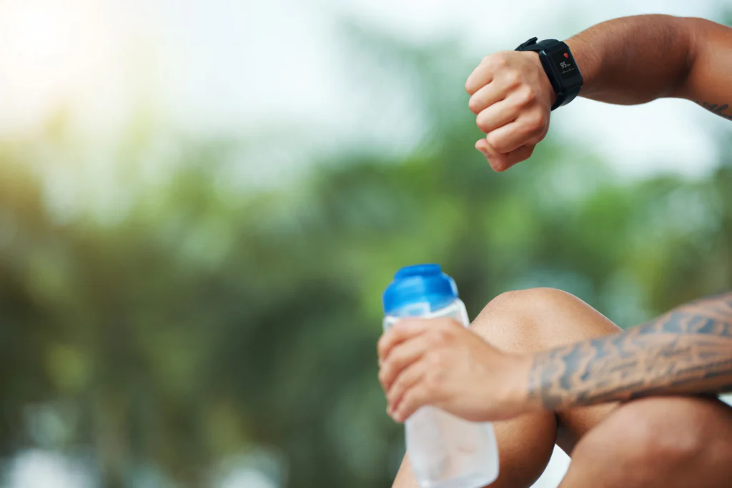 A runner resting with a water bottle and sports watch to monitor post marathon recovery