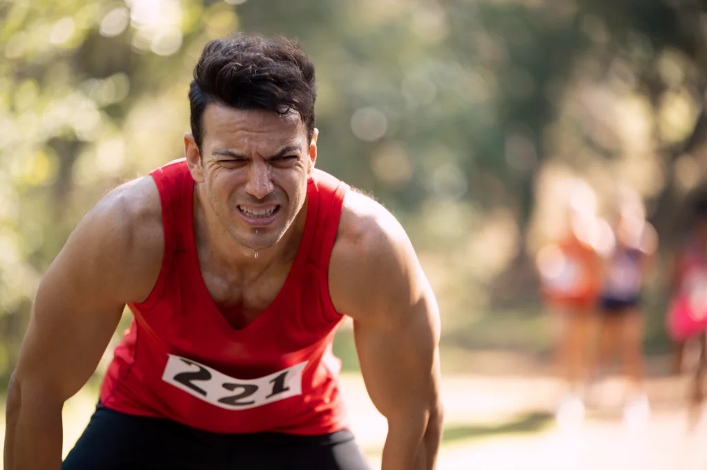 Sweaty and exhausted runner with a race bib focused on marathon recovery after the race.