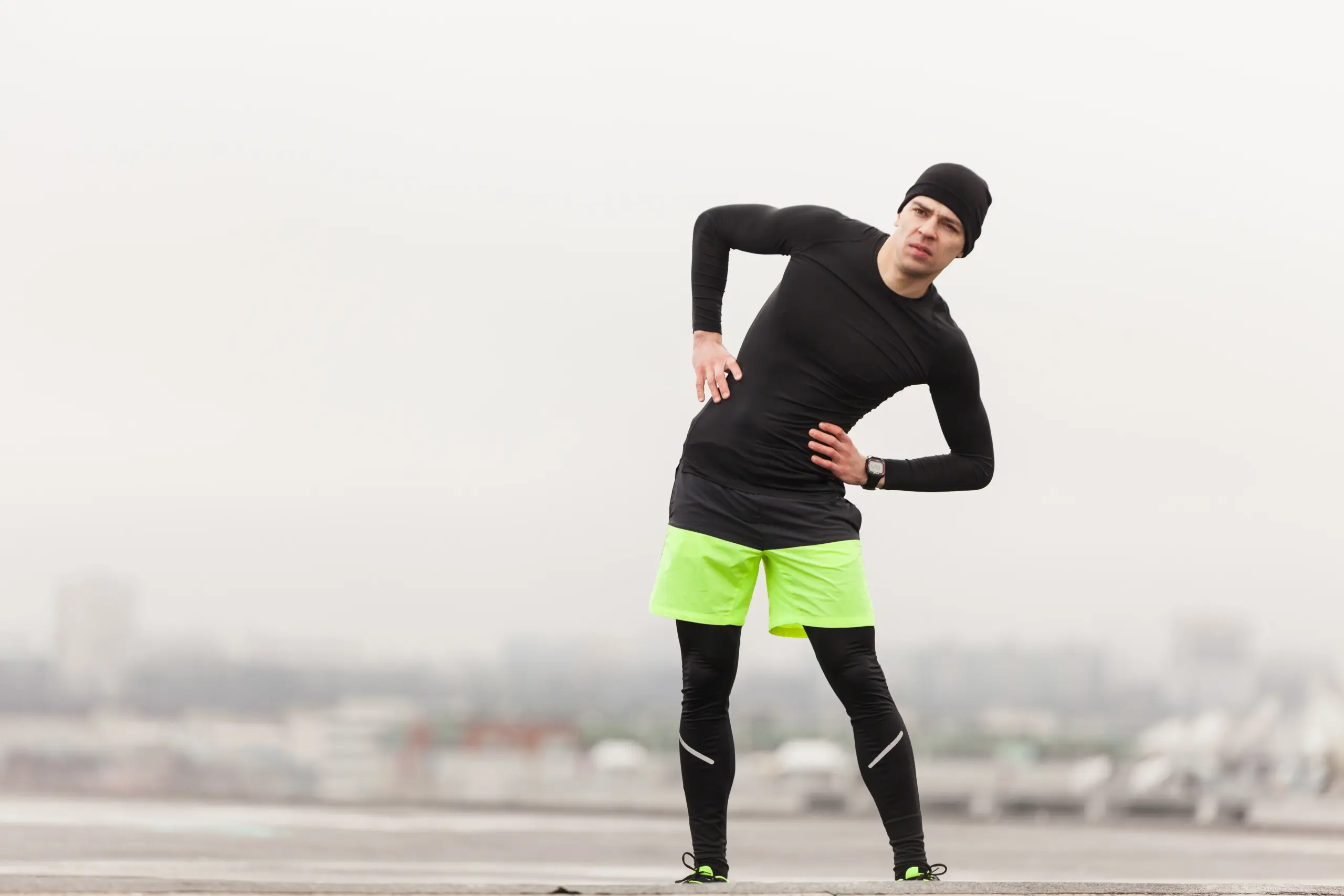 A male runner holding his hip while stretching, showing signs of deep inner hip pain.